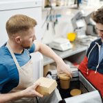 Dois funcionários preparam pedidos de delivery em uma cozinha de restaurante.