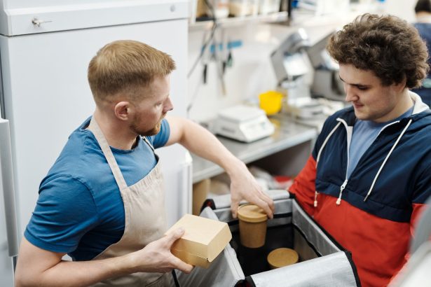 Dois funcionários preparam pedidos de delivery em uma cozinha de restaurante.