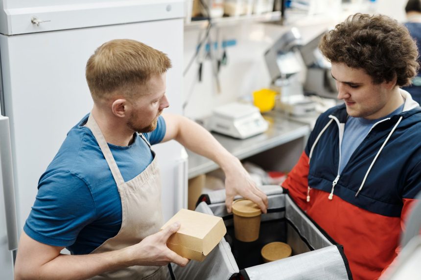 Dois funcionários preparam pedidos de delivery em uma cozinha de restaurante.