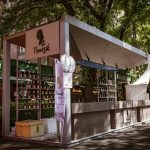 Barraca de vinhos em uma feira ao ar livre, cercada por árvores e visitantes.