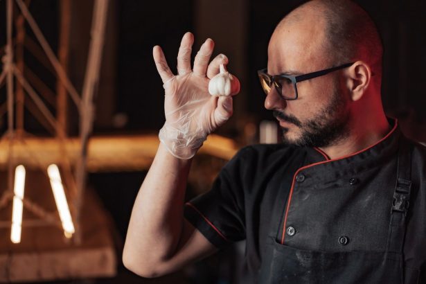 Chef usando luvas e óculos segura um dente de alho em uma cozinha.