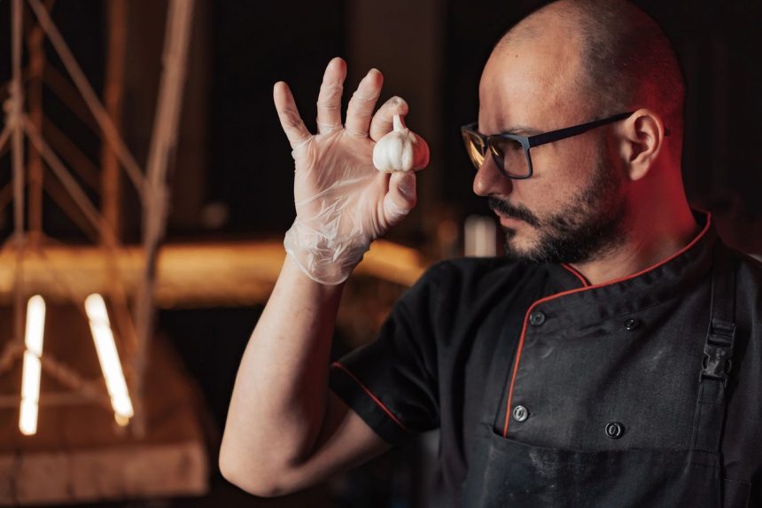 Chef usando luvas e óculos segura um dente de alho em uma cozinha.