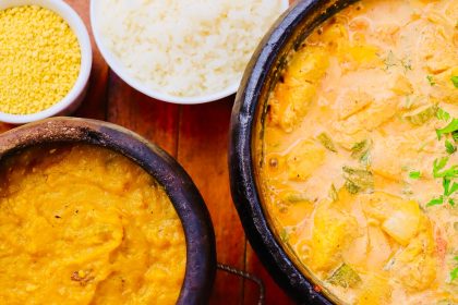 Moqueca brasileira colorida servida em panela de barro, acompanhada de outros pratos sobre uma mesa de madeira
