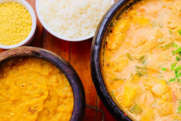 Moqueca brasileira colorida servida em panela de barro, acompanhada de outros pratos sobre uma mesa de madeira