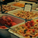 Buffet com saladas, carnes e pimentões recheados dispostos em travessas.