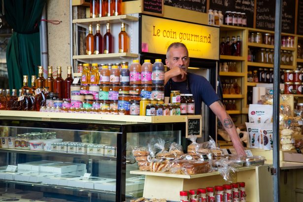 Comerciante diante de uma banca de feira com diversos produtos gourmet expostos.