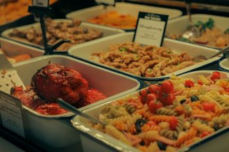 Buffet com saladas, carnes e pimentões recheados dispostos em travessas.