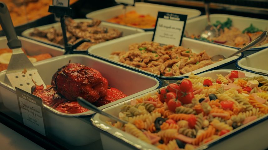 Buffet com saladas, carnes e pimentões recheados dispostos em travessas.